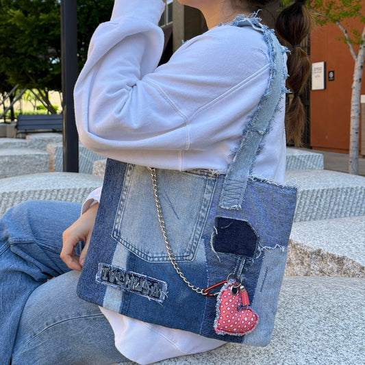 Woman wearing the Denim Tangerine Bag on her shoulder while seated outdoors, showcasing its compact size, raw textures, and unique patchwork design.