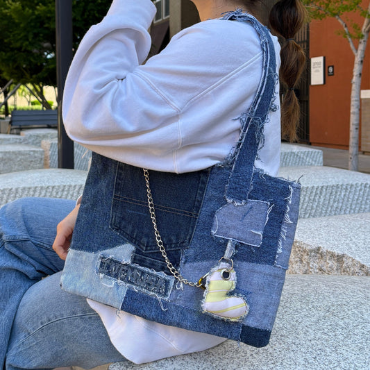 Model sitting on outdoor bench holding the Denim Yellow Handbag with yellow heart charm and visible chain strap in a streetwear outfit