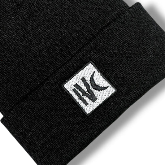 Close-up of IVENUSA black knit beanie featuring minimalist white square IVC logo patch stitched on the cuff.