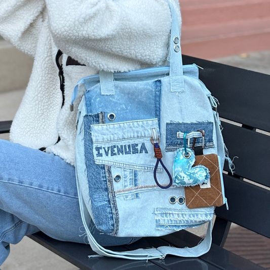 Model sitting on a bench with IVENUSA light-wash upcycled denim tote bag featuring mixed patchwork and unique handmade keychains.