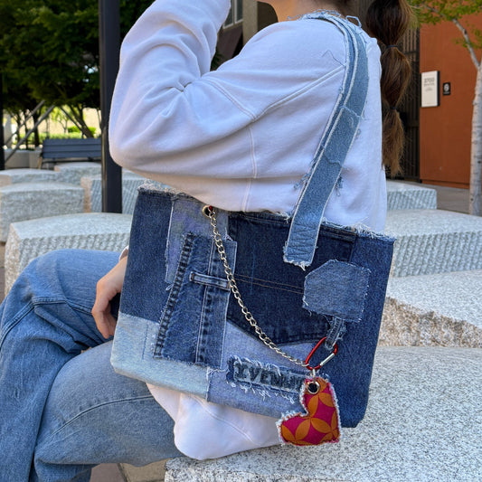 Woman sitting outdoors holding the Denim Red Handbag over her shoulder, showing patchwork front and red heart charm.