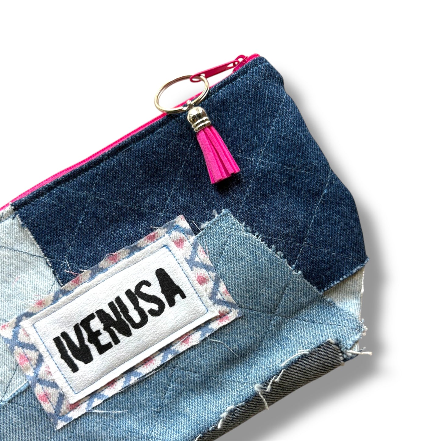 Close-up of IVENUSA patchwork denim makeup bag showing stitched logo, pink tassel zipper pull, and quilted texture