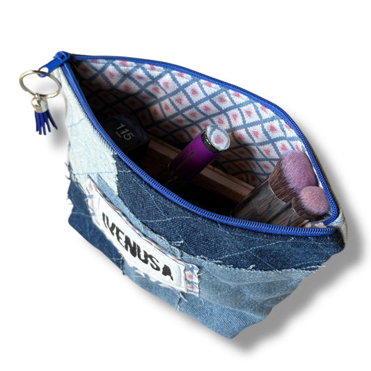 Open patchwork denim makeup bag showing pink and blue striped lining, blue zipper, and stored cosmetics
