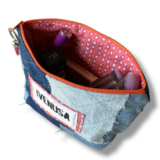 Open patchwork denim makeup bag showing white and orange squares, zipper, and stored cosmetics