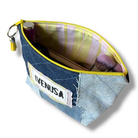 Open patchwork denim makeup bag showing pink and yellow striped lining, zipper, and stored cosmetics