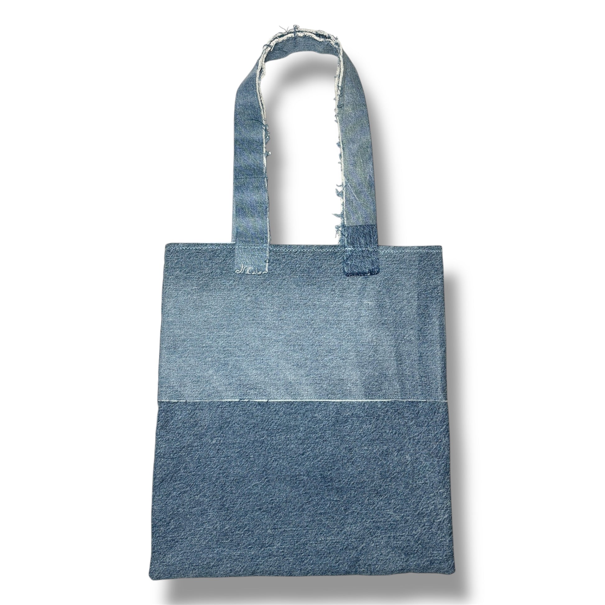 Back view of the A Susurros Suaves Tote bag showing clean dual-tone denim design and frayed strap edges.