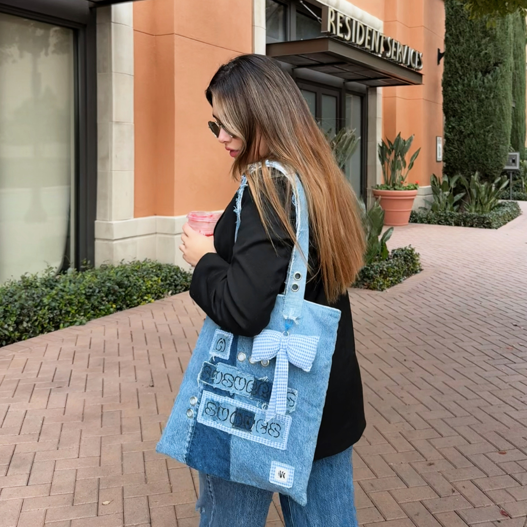 Woman holding a pink drink, walking with the A Susurros Suaves Tote bag in a casual urban setting.