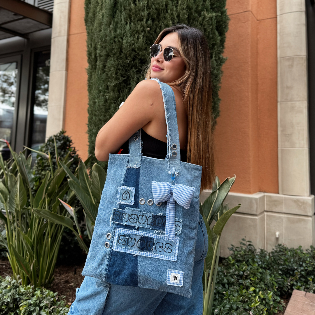 Woman wearing the A Susurros Suaves Tote bag on her shoulder, styled with sunglasses and denim-on-denim outfit in a city environment.