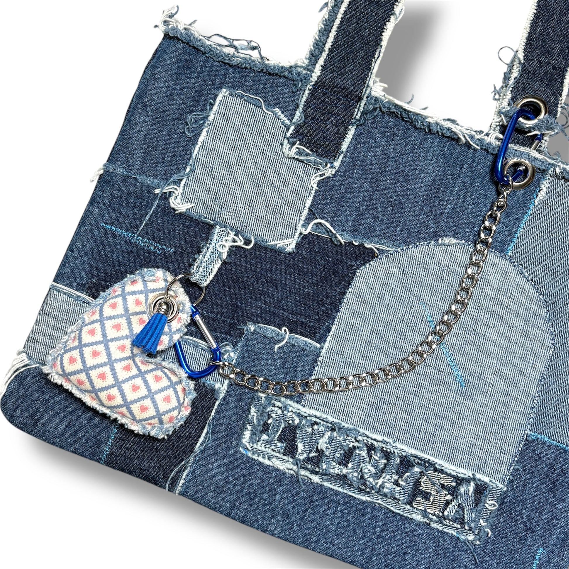 Close-up of denim handbag showcasing textured patchwork, heart charm with blue carabiner, and silver chain attachment.