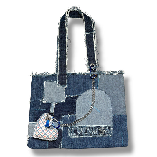 Upcycled blue denim handbag featuring frayed patchwork design, front chain detail, and heart-shaped charm.