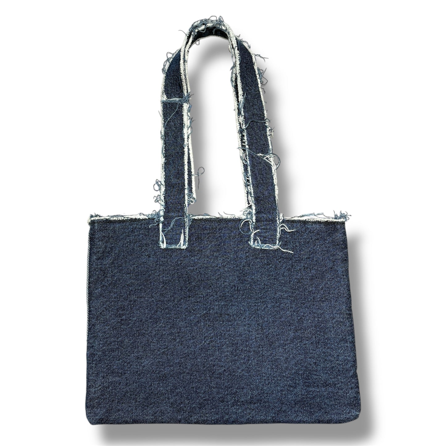 Backside of frayed-edge blue denim tote bag with minimalist dark wash finish and distressed straps.
