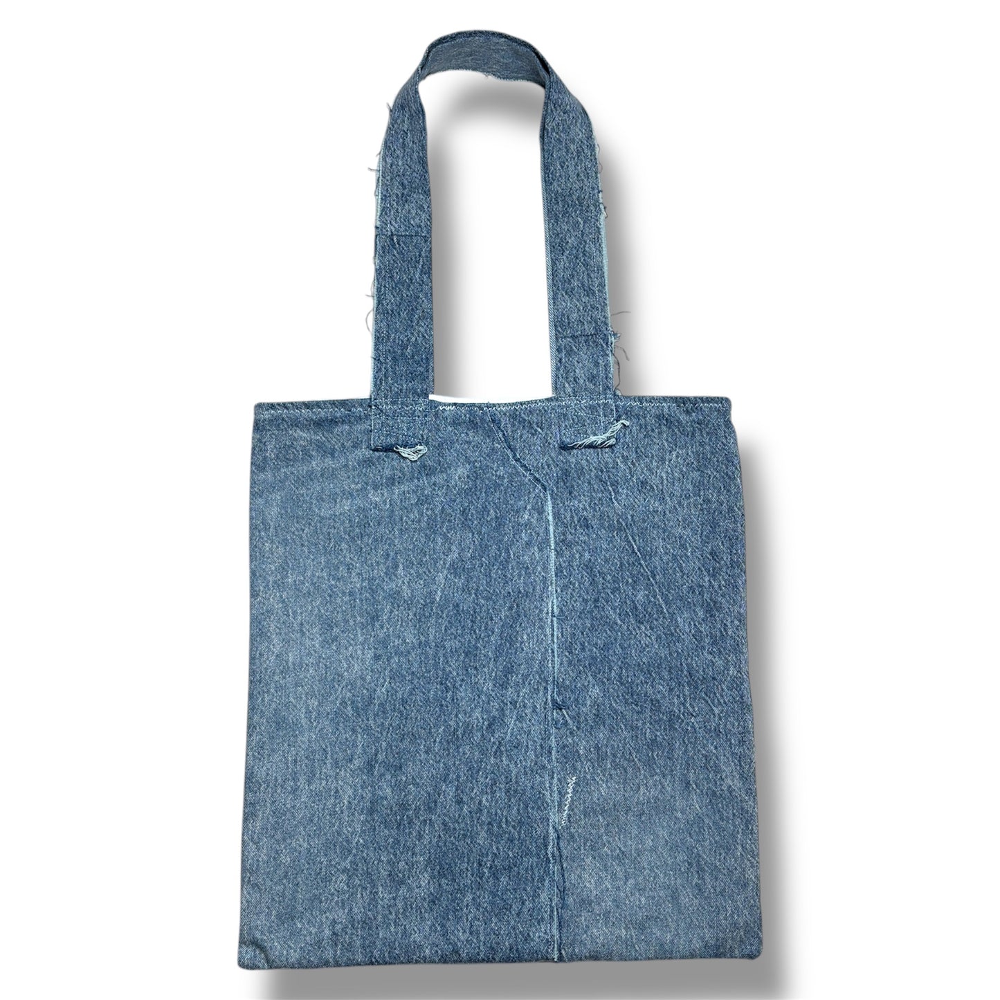 Rear view of the Cada Vez Que Me Miras tote bag with a clean, two-tone denim panel design and reinforced stitched handles.