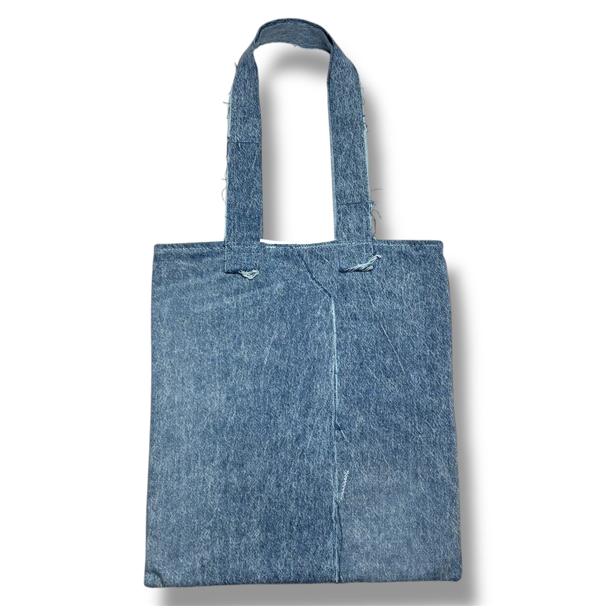 Rear view of the Cada Vez Que Me Miras tote bag with a clean, two-tone denim panel design and reinforced stitched handles.