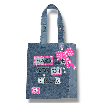Full front view of the Cada Vez Que Me Miras tote bag made of upcycled denim, featuring stitched phrases and a pink polka dot bow on the handle.