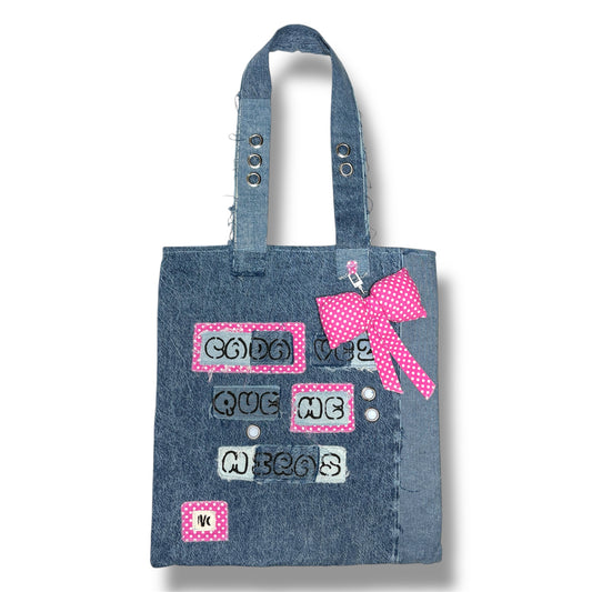 Full front view of the Cada Vez Que Me Miras tote bag made of upcycled denim, featuring stitched phrases and a pink polka dot bow on the handle.
