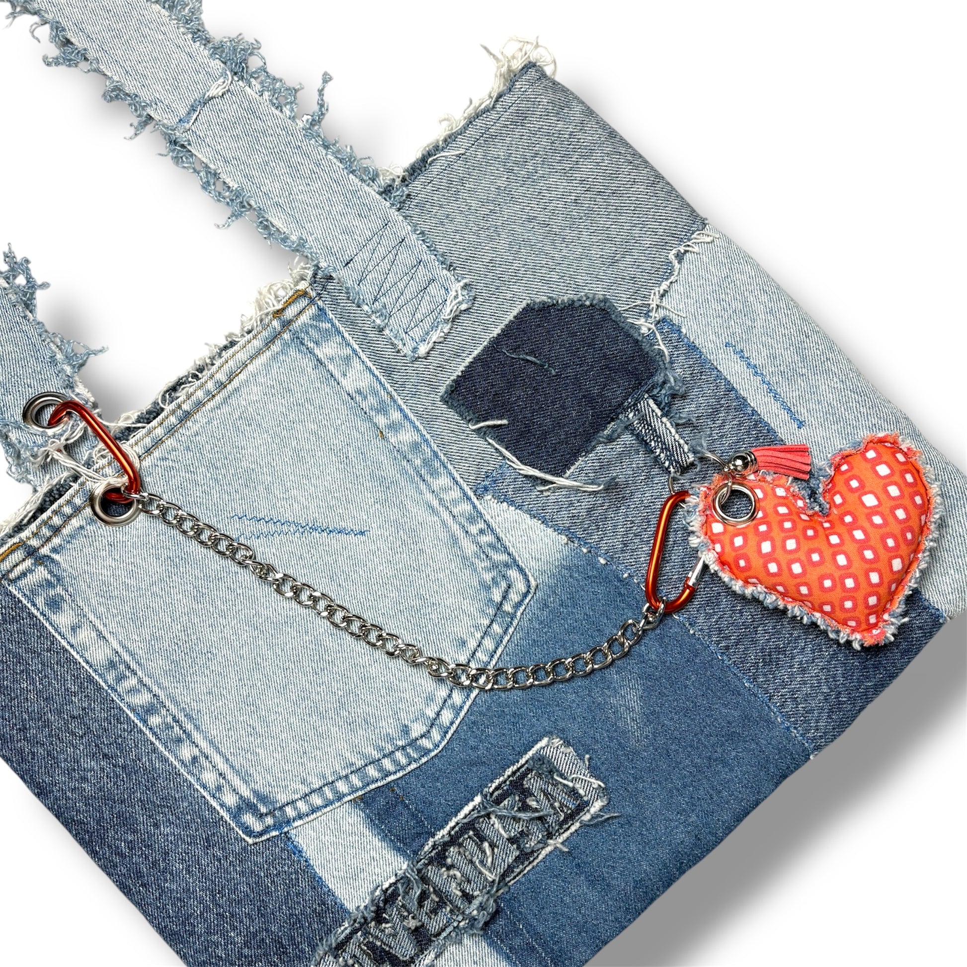 Front view of the Denim Tangerine Bag featuring raw-edge patchwork, a repurposed denim pocket, silver chain, and a red-orange heart keychain accessory.