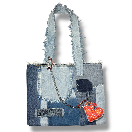 Full front shot of the Denim Tangerine Bag made from mixed-wash denim patches, complete with frayed handles, a chain detail, and bold heart charm.