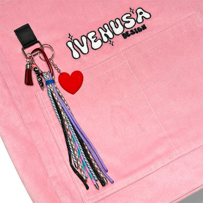 Close-up of IVENUSA embroidered logo on Rosé Avenue Bag with red heart charm and colorful tassel keychain attached to front pocket.