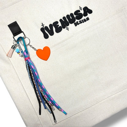 Close-up of IVENUSA’s embroidered logo on the Rush Hour Bag, featuring a playful orange heart charm and colorful string tassel keychain.