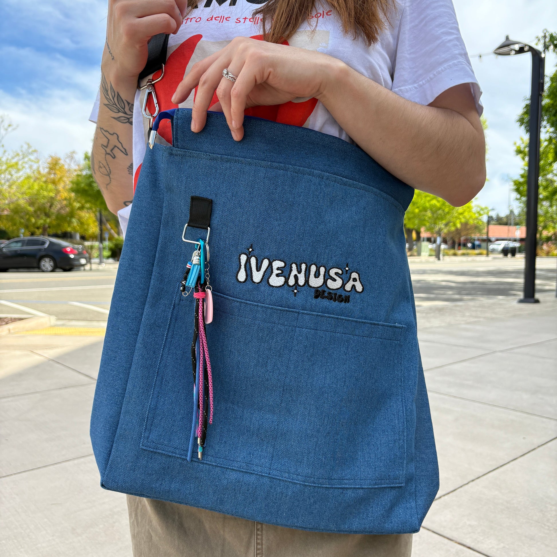 Model carrying the Skyline Bag across one shoulder, showcasing the IVENUSA logo and colorful keychain in a laid-back city streetwear vibe.
