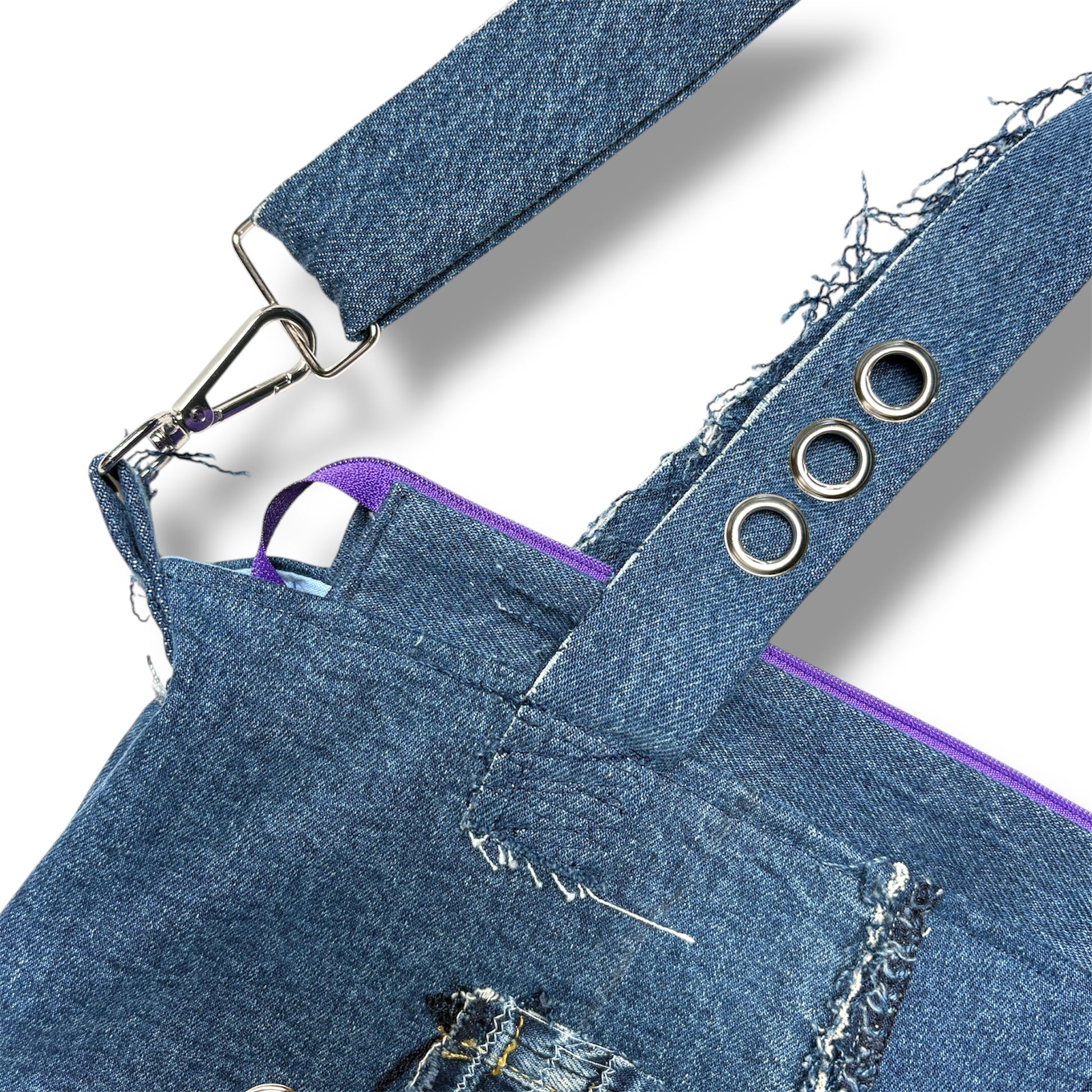 Close-up of adjustable denim strap with silver grommets and purple zipper lining on handcrafted tote bag.