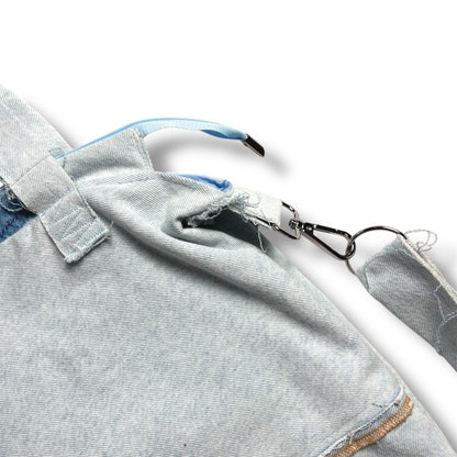 Close-up of IVENUSA light-wash tote bag showing raw-edge seamwork, baby blue zipper, and detachable shoulder strap hardware.