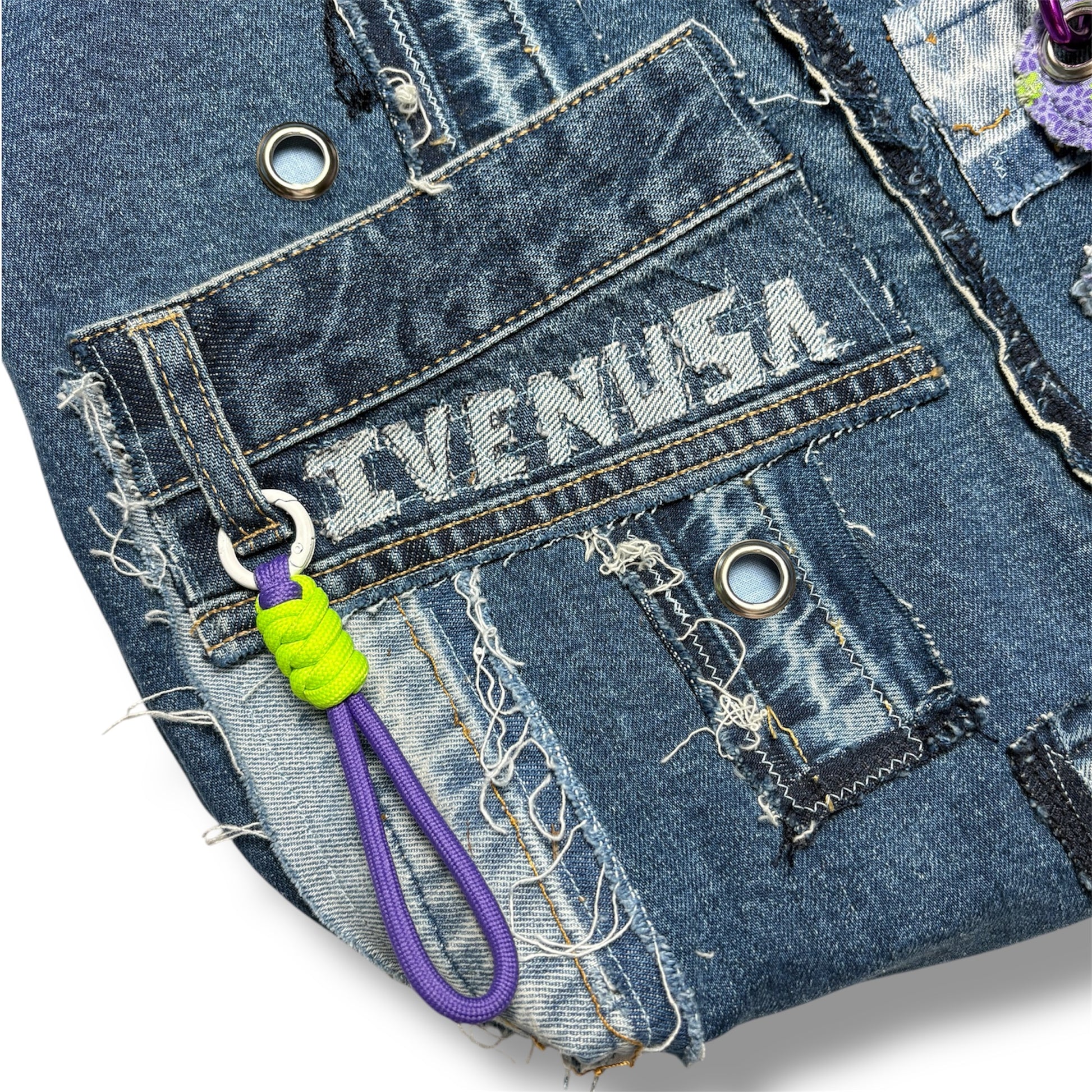 Detail of front utility pocket and IVENUSA embroidered logo on repurposed denim tote bag with neon and purple keychain.