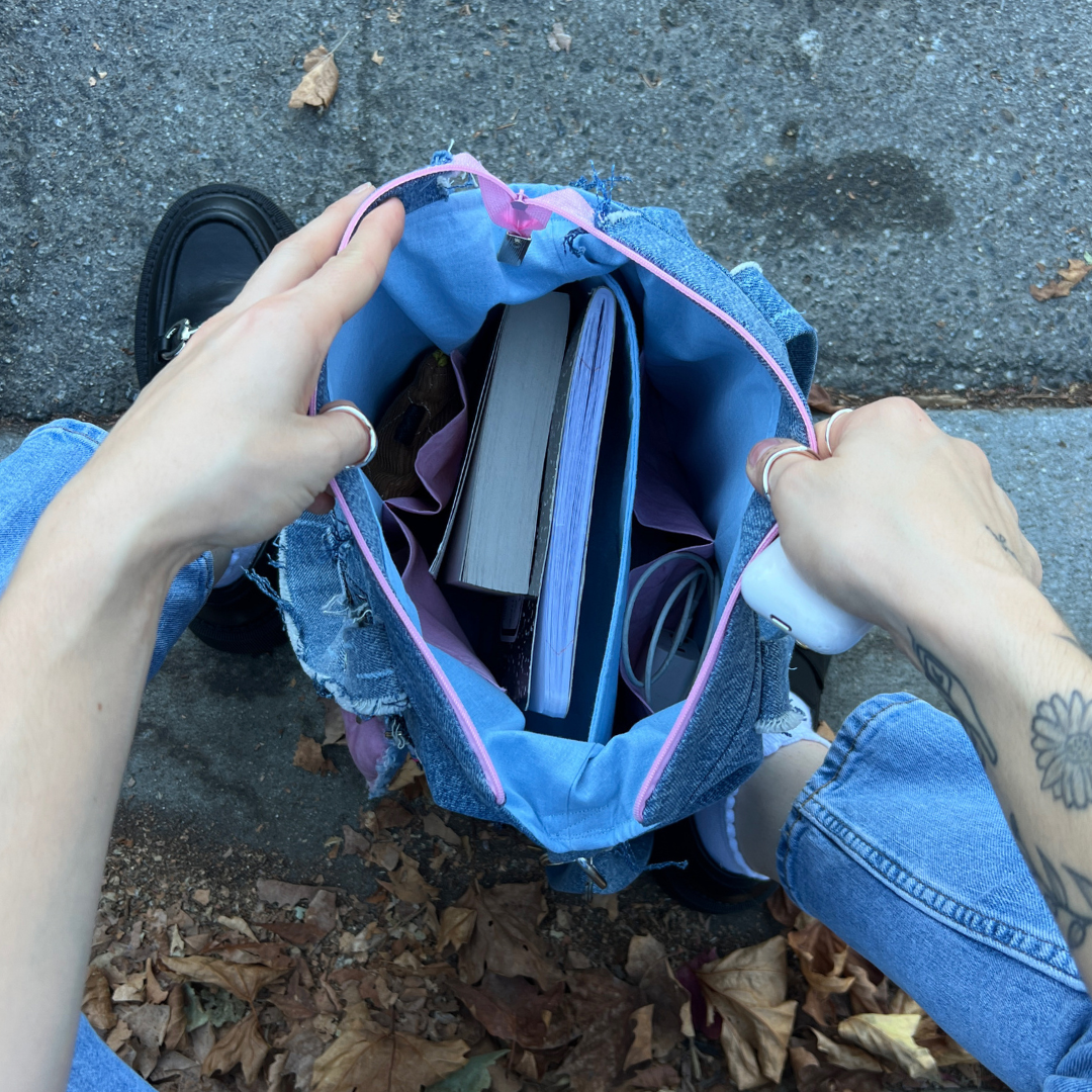 Top view of person holding open an IVENUSA upcycled denim tote bag filled with books and daily essentials, showcasing spacious interior with pink lining.
