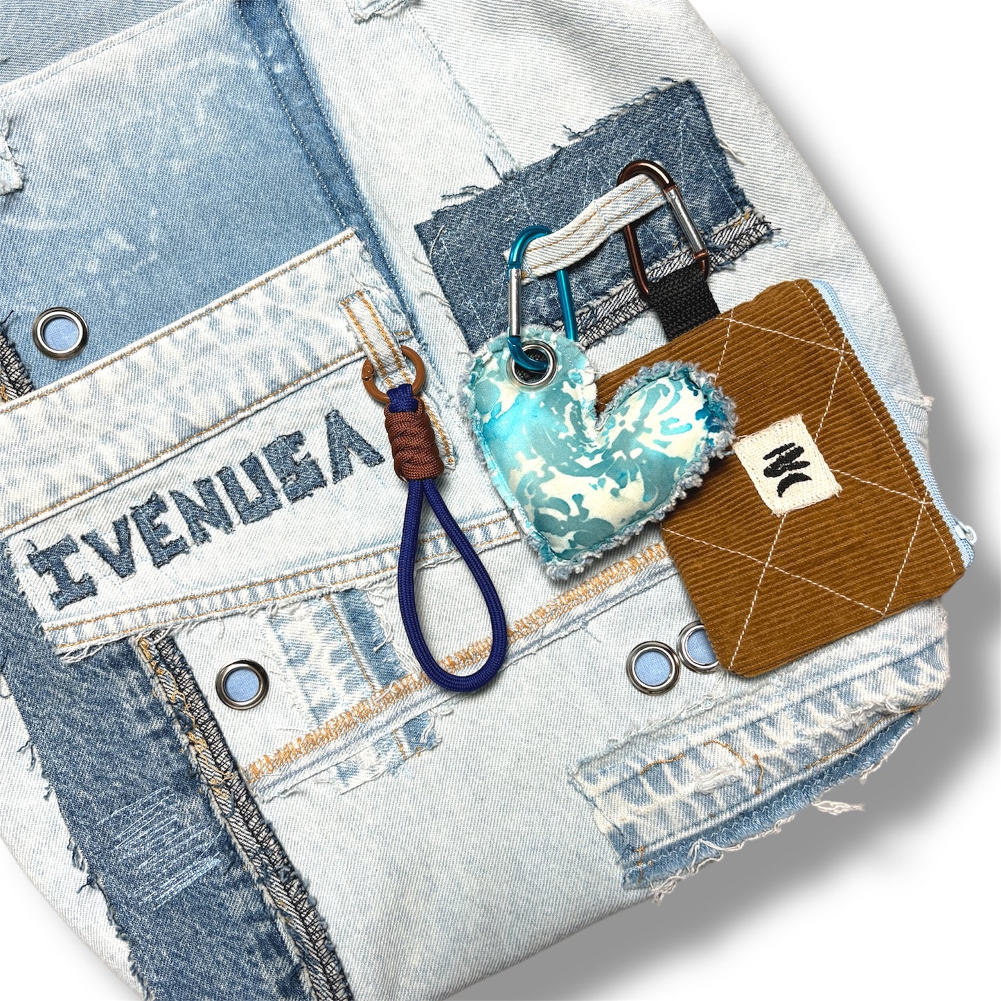 Detail of brown corduroy coin pouch and turquoise heart keychain clipped to IVENUSA light denim tote with signature embroidery.