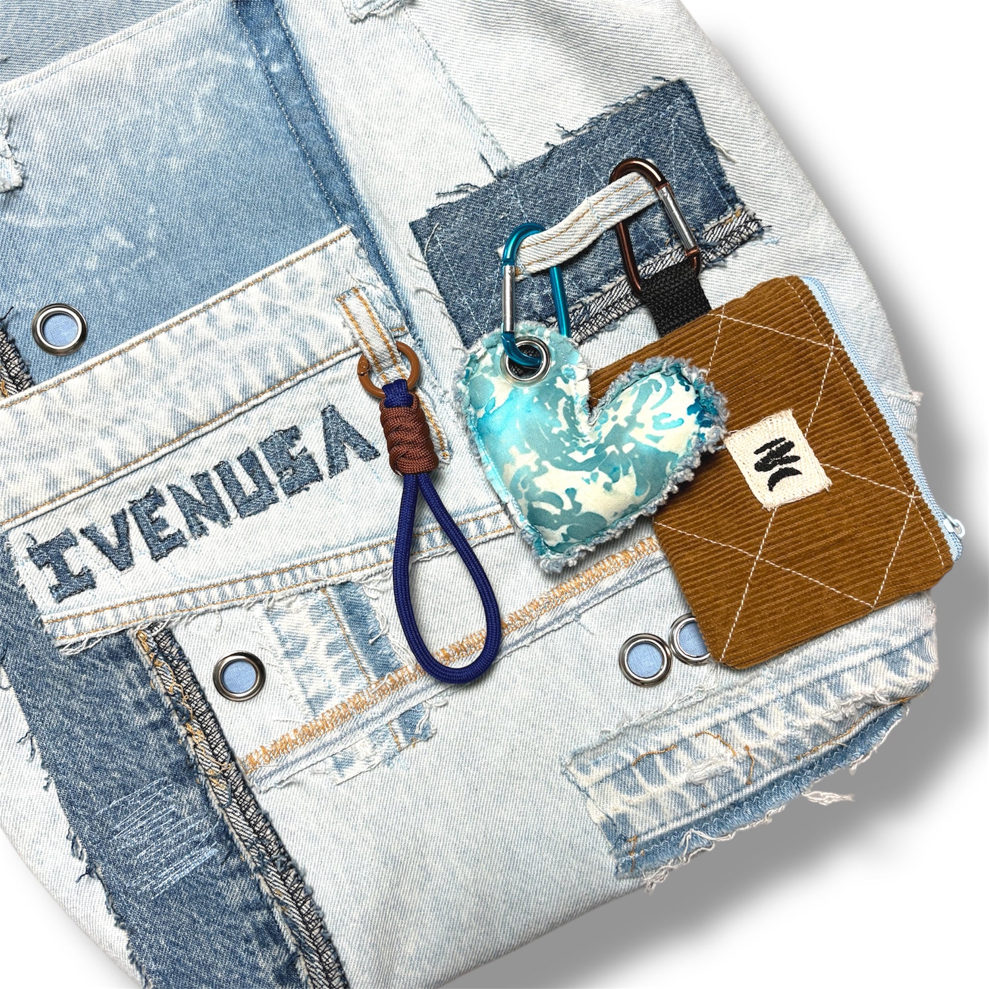 Detail of brown corduroy coin pouch and turquoise heart keychain clipped to IVENUSA light denim tote with signature embroidery.