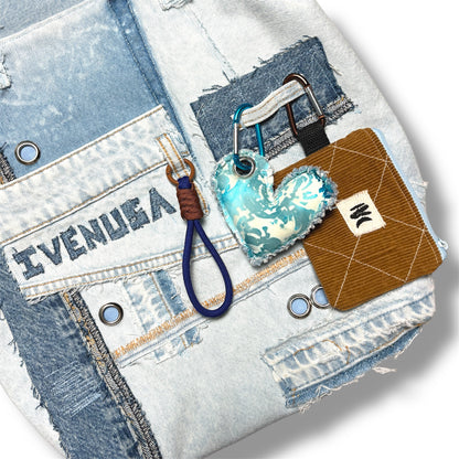 Detail of brown corduroy coin pouch and turquoise heart keychain clipped to IVENUSA light denim tote with signature embroidery.
