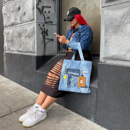 Model seated by a city wall, styling the Iconic Yellow denim tote with visible heart keychain and utility pouch.