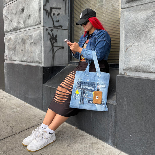 Model seated by a city wall, styling the Iconic Yellow denim tote with visible heart keychain and utility pouch.