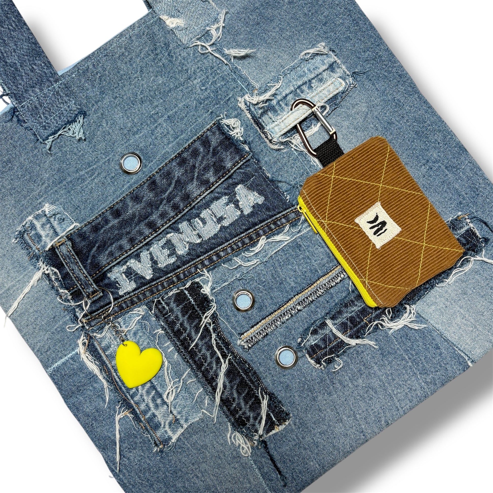 Zoomed-in detail of the Iconic Yellow tote's front pocket, chain, yellow heart charm, and pouch attached to the handle.