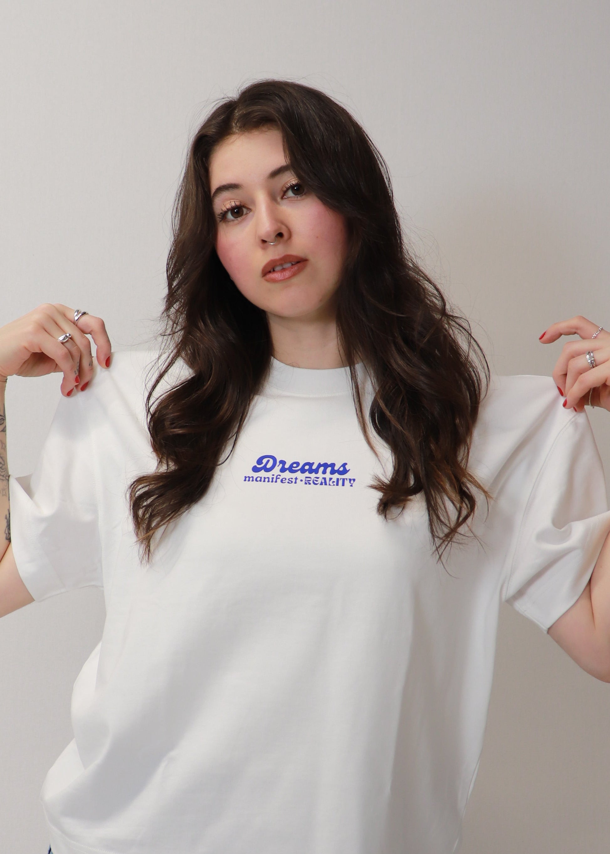 Female model holding white DMR oversized tee showing front logo detail