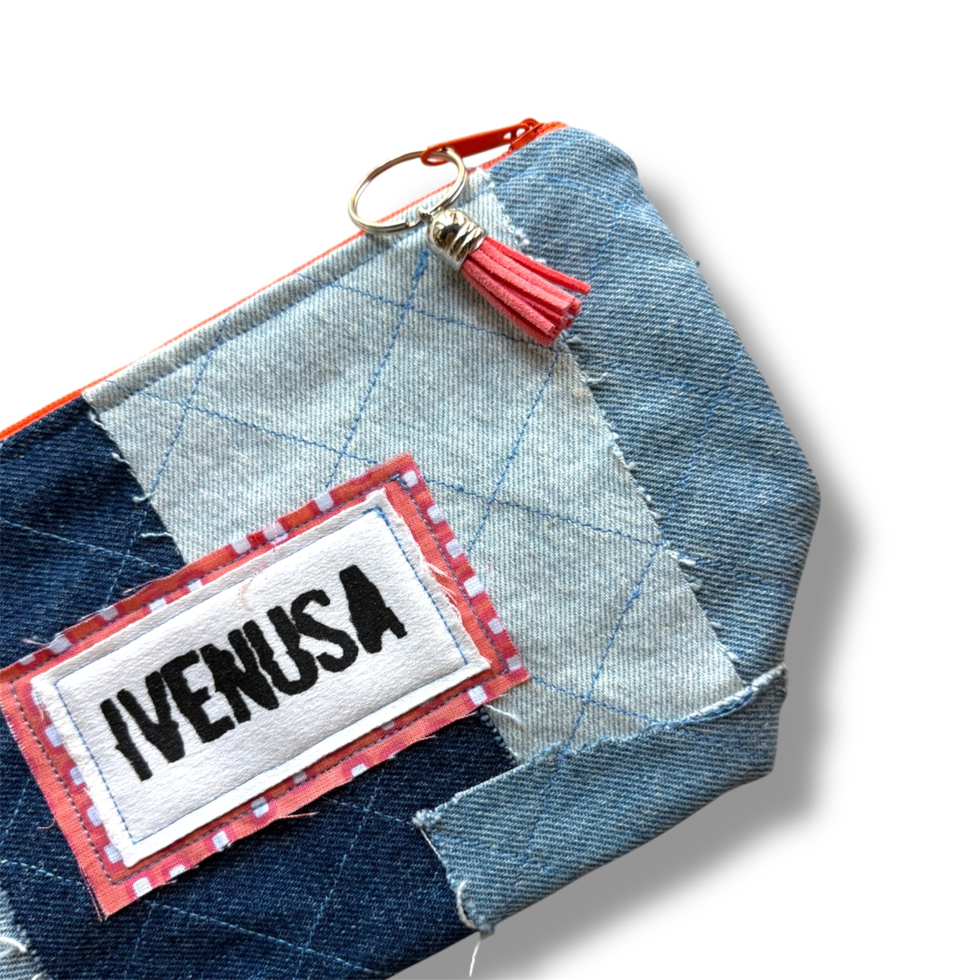 Close-up of IVENUSA patchwork denim makeup bag showing stitched logo, orange tassel zipper pull, and quilted texture