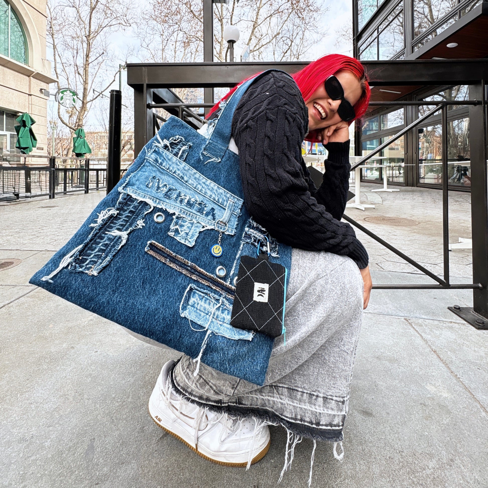 Young woman with red hair in grey skirt and black hoodie wearing Ivenusa patchworked denim tote bag with black wallet in downtown