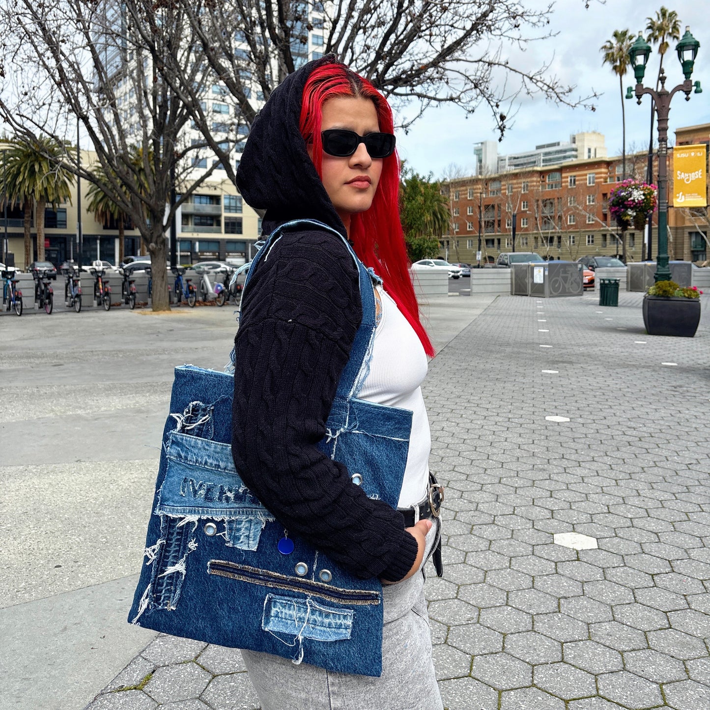 Young woman with red hair in grey skirt, white and black hoodie wearing Ivenusa patchworked denim tote bag with black wallet in downtown